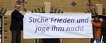 Bischof Thomas Adomeit (li.) und Birgit Carmona Scheider vom Bischofsbüro befestigen das Banner mit den Psalmworten „Suche Frieden und jage ihm nach!“ (Psalm 34,15) am Gebäude des Oberkirchenrates im Oldenburger Philosophenweg. Foto: ELKiO/D.-M. Grötzsch